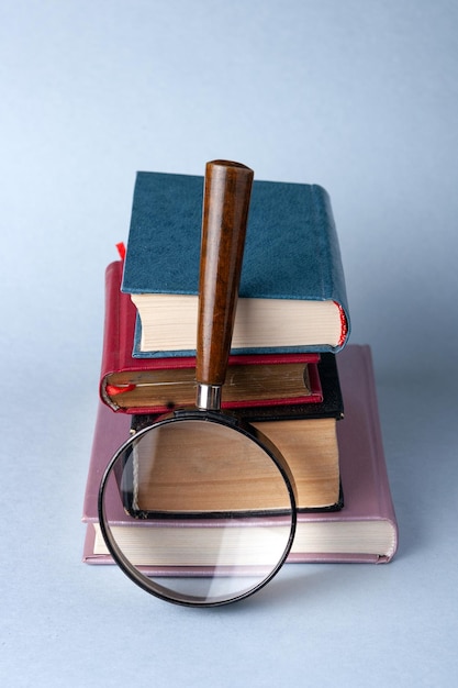 Une pile de livres à couverture rigide et une loupe sur fond bleu