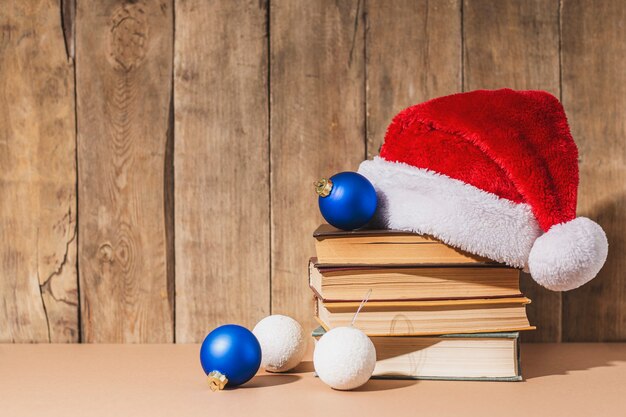 Photo pile de livres, décorations d'arbre de noël et chapeau de père noël sur fond en bois.