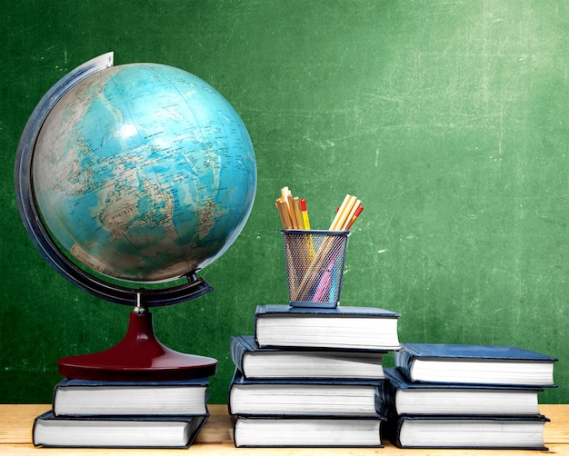 Pile de livres et globe avec des crayons dans un panier sur la table en bois