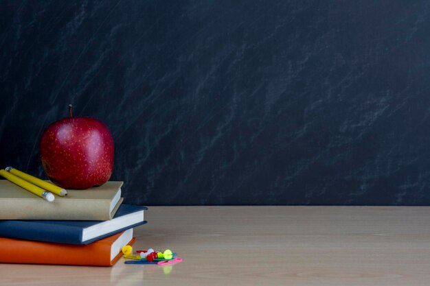 Une pile de livres une pomme rouge et des fournitures scolaires colorées sur un fond noir du tableau noir avec un endroit pour l'inscription