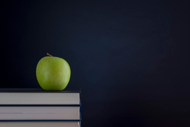 Une pile de livres avec une pomme verte sur le bureau sur un fond noir du tableau noir avec un endroit pour l'inscription