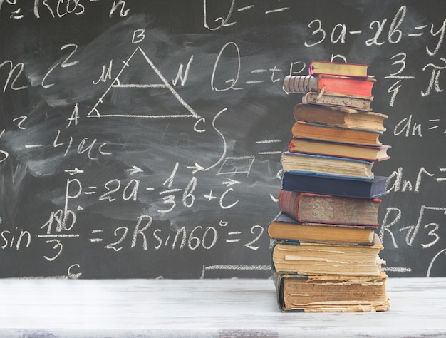 Pile de livres sur table en bois blanc avec des formules mathématiques sur tableau noir