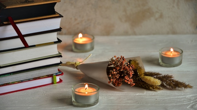 Pile de livres, trois bougies et fleurs séchées sur un fond en bois blanc. Fond d'automne. Vue de côté. Fermer. Mise à plat.