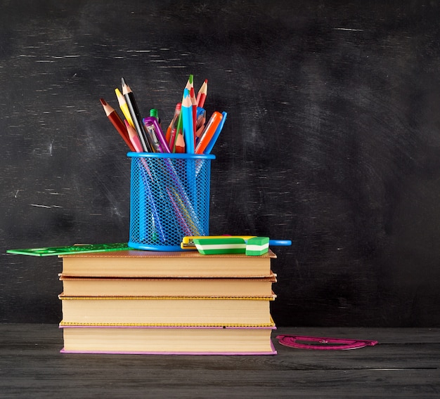 Pile de livres et un verre de papeterie bleu avec des crayons en bois multicolores