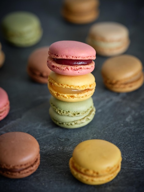 Pile de macarons savoureux et sucrés fraîchement sortis du four avec différentes saveurs placés sur une table grise dans une pièce lumineuse sur fond flou