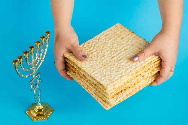 Une pile de matzo dans les mains des femmes sur une surface bleue à côté d'un verre de vin menorah