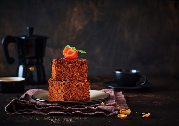 Pile de morceaux ou barre de brownie au gâteau au chocolat avec des fraises et des pistaches sur le fond noir, image de mise au point sélective.