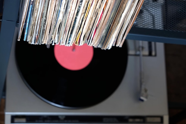Pile de nombreux disques vinyles debout dans de vieilles couvertures et platine dans un boîtier gris sur un bureau