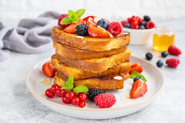 Une pile de pain perdu sur une assiette avec des baies fraîches, des pétales d'amande et du miel sur un fond de béton gris. Petit déjeuner délicieux. Espace de copie.