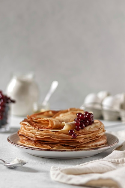 Une pile de pancakes avec une sauce aux fruits rouges et un pot de yaourt.