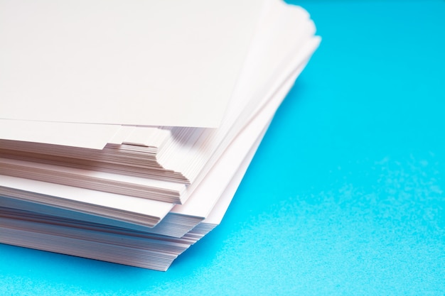 Photo une pile de papier blanc sur une table sur un fond bleu. pages vierges prêtes à être imprimées et imprimées.