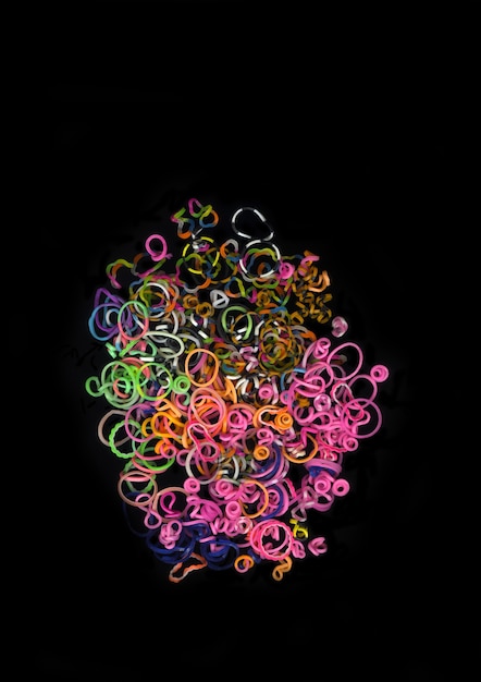 Pile de petites bandes de caoutchouc colorées rondes pour faire des bracelets de métier à tisser arc-en-ciel isolés sur fond sombre