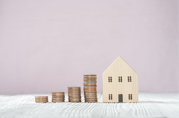 Pile de pièces d'argent avec modèle de maison en bois sur fond de bois blanc