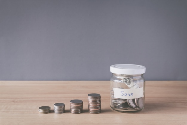 Pile de pièces et de pièces dans un bocal en verre sur un bureau en bois, concept d'économie d'argent