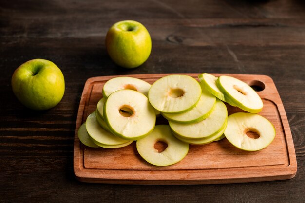 Pile de pommes vertes fraîches prêtes à être mises sur un séchoir à fruits sur une planche à découper en bois et deux granny smiths à proximité sur la table de cuisine