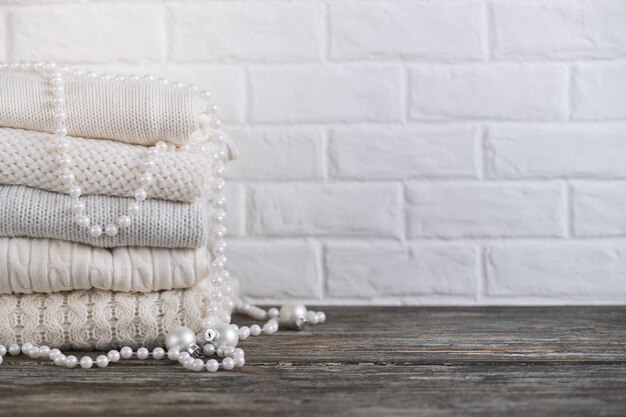 Pile de pulls et de perles tricotés confortables blancs sur une table en bois. Espace pour le texte.