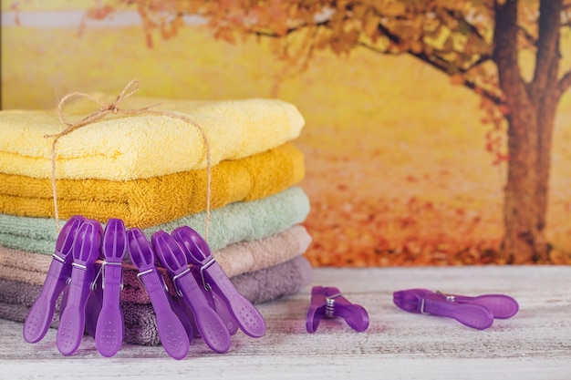 Pile de serviettes de bain colorées avec pinces à linge violettes sur planche de bois clair. Dans l'arbre d'automne de fond. Serviettes en coton aux couleurs pastel. Concept hygiène, tissu, spa et textile