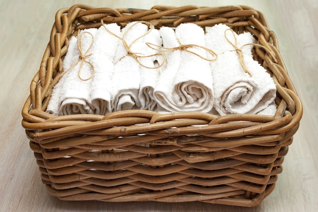 Pile de serviettes éponge roulée blanche propre dans un panier en osier dans un panier en bois naturel. Fermer. Flou sélectif. Espace de copie de texte.
