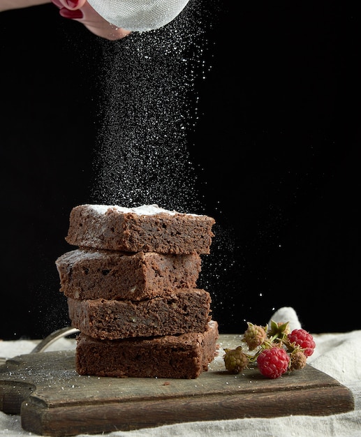 Pile de tranches de gâteau au chocolat brownie cuites au four, saupoudrées de sucre blanc provenant d'un tamis en fer