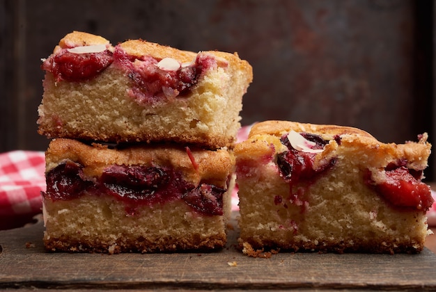 Pile de tranches de gâteau éponge au four carré avec des prunes sur planche de cuisine en bois