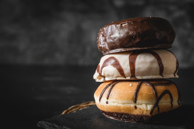 Pile de trois beignets frais différents avec glaçage au chocolat et au caramel sur une planche de bois