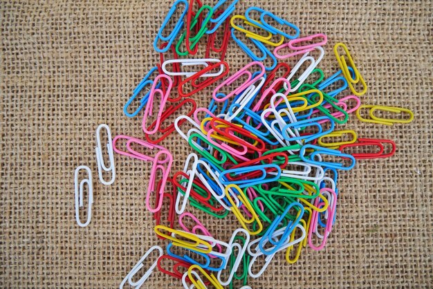 Une pile de trombones colorés se trouve sur un sac en toile de jute.