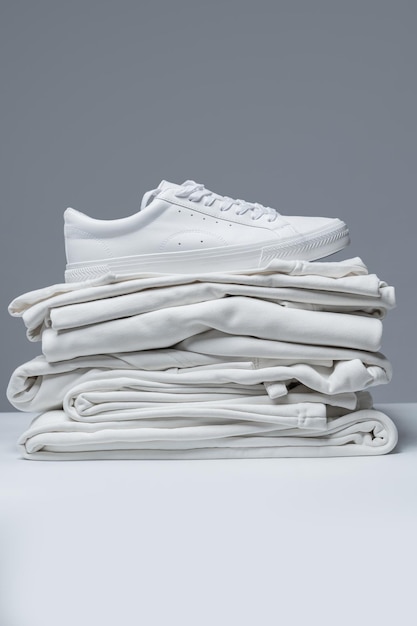 Pile de vêtements blancs et de baskets élégantes sur fond gris