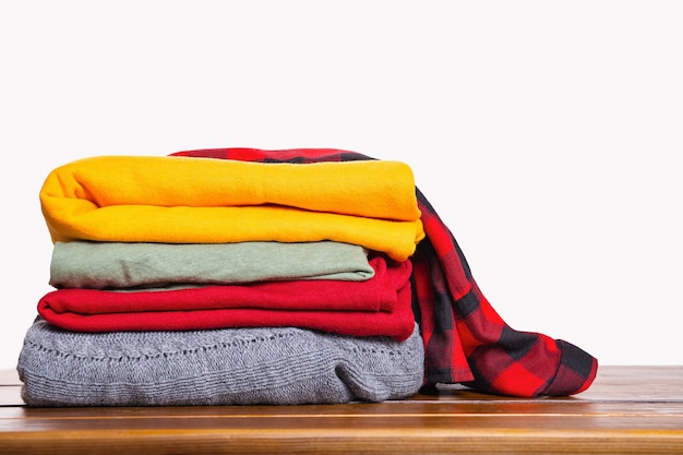 Une pile de vêtements d'hiver automne plié sur une table en bois sur fond blanc.