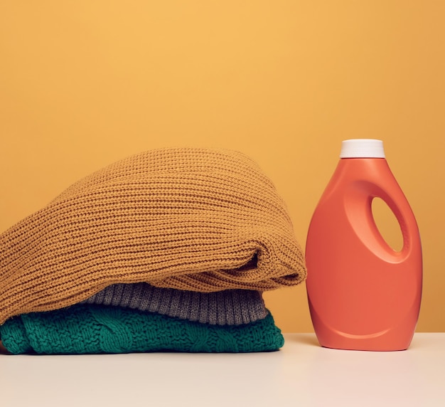 Pile de vêtements pliés lavés et grande bouteille orange en plastique avec support de détergent liquide sur un tableau blanc fond jaune Devoirs de routine