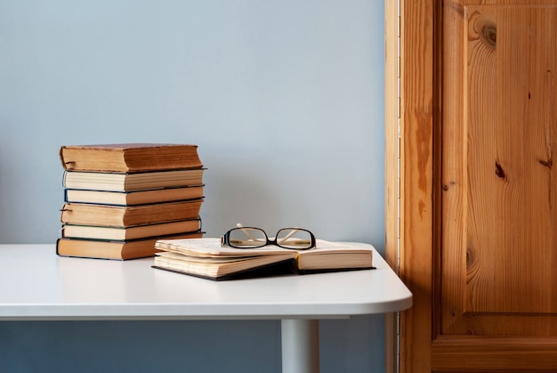 Pile de vieux livres sur une table blanche, un livre est ouvert avec des verres sur le dessus.