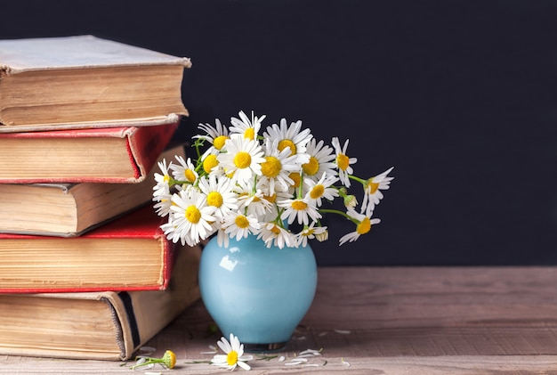 Une pile de vieux livres vintage se trouvant sur une étagère en bois avec un bouquet de marguerites.