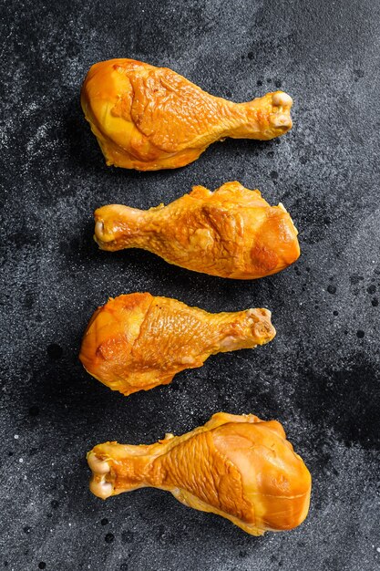 Pilons de cuisse de poulet fumé épicé sur une table de cuisine. Fond noir. Vue de dessus.