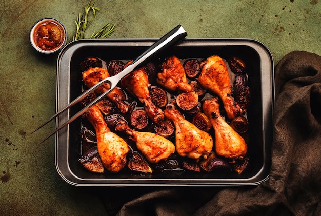 Pilons de cuisses de poulet au four avec figues et oignons rouges dans une marinade balsamique dans un plat de cuisson en céramique vue de dessus sur fond blanc