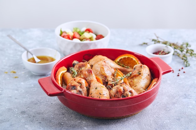 Photo pilons de poulet aux oranges et au thym cuits dans un plat de cuisson rond rouge