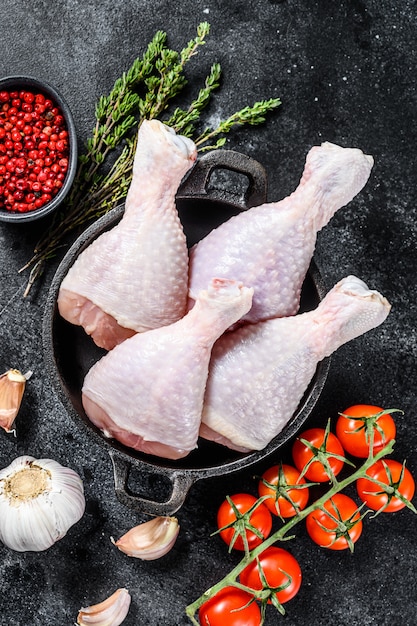 Pilons de poulet cru, cuisses aux herbes et épices dans une casserole. Viande de volaille biologique. Fond noir. Vue de dessus