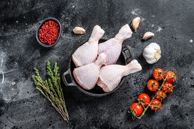 Pilons de poulet cru, cuisses aux herbes et épices dans une casserole. Viande de volaille biologique. Fond noir. Vue de dessus