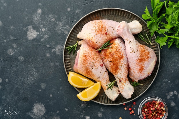 Pilons de poulet cru avec des ingrédients pour la cuisson sur une surface en pierre noire. Vue de dessus.