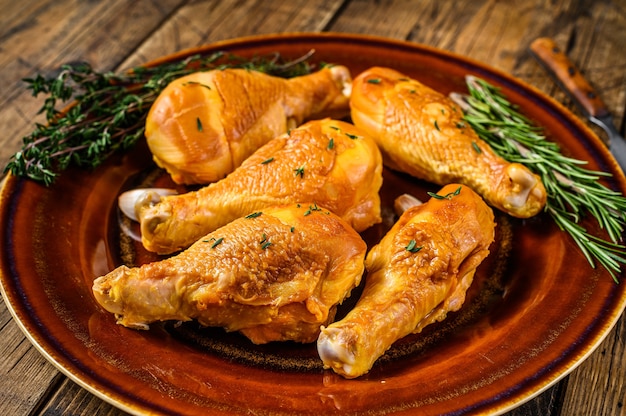 Pilons de poulet fumés frais sur une assiette rustique avec des herbes. fond en bois. Vue de dessus.