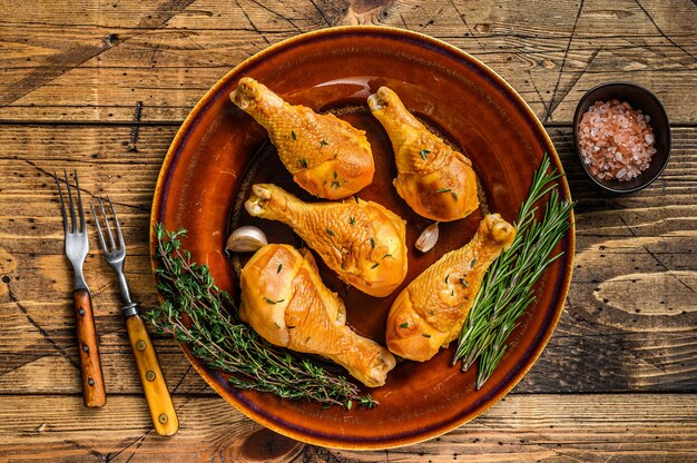 Pilons de poulet fumés frais sur une assiette rustique avec des herbes. fond en bois. Vue de dessus.