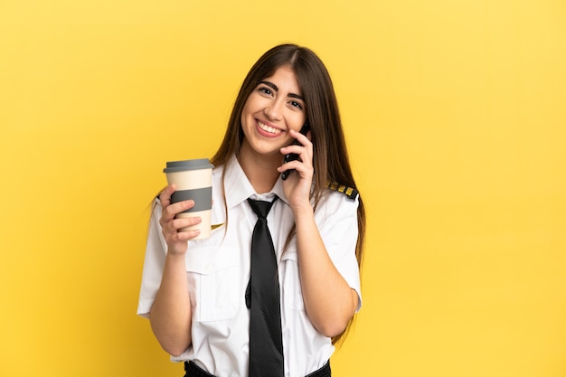 Pilote d'avion isolé sur un mur jaune tenant du café à emporter et un mobile