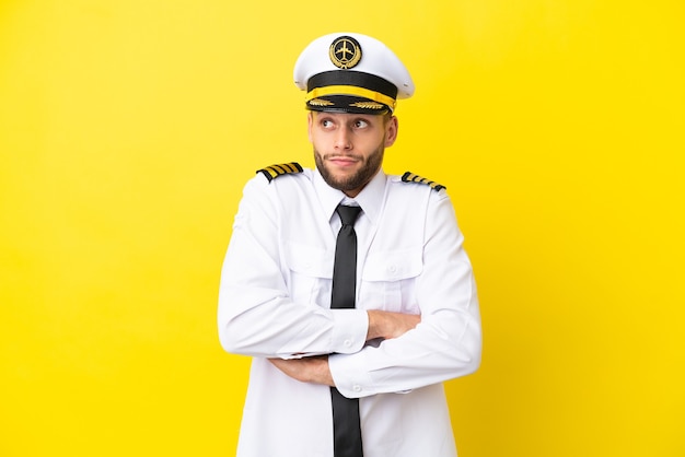 Pilote caucasien d'avion isolé sur fond jaune faisant un geste de doute tout en soulevant les épaules