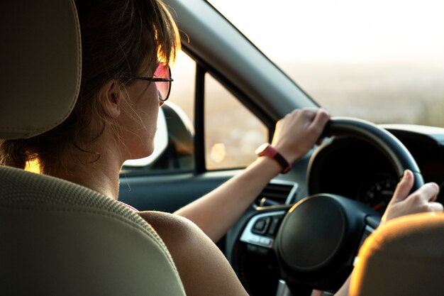 Pilote femme tenant le volant conduisant une voiture au coucher du soleil