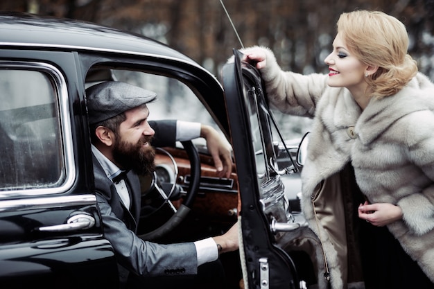 Pilote homme avec femme en manteau de fourrure couple vintage à la voiture rétro noire