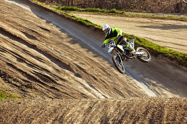 Photo un pilote de motocross en action accélérant la moto décolle et saute sur le tremplin de la course