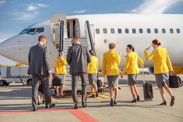 Pilotes masculins et hôtesses de l'air en uniforme d'aviation debout près de l'avion à l'aérodrome