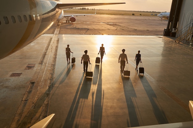 Pilotes non reconnus et hôtesses de l'air marchant près de l'avion de passagers avec leurs valises