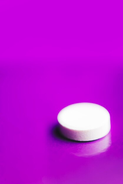 Une pilule blanche sur un fond lilas solide avec réflexion
