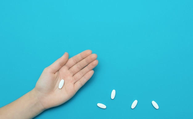 Pilule blanche en main et quelques pilules sur fond bleu. Concept de médecine.