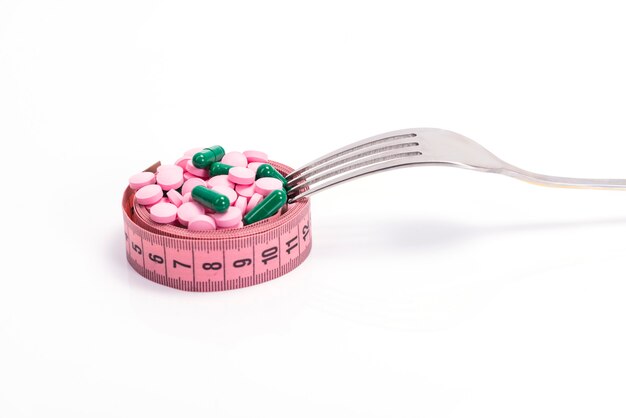 Pilules amaigrissantes multicolores et suppléments tels que des aliments sur une assiette sous la forme d'un ruban centimétrique avec une fourchette