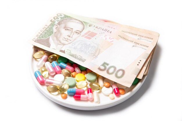 Pilules et argent ukrainien sur fond blanc. Le concept de la hausse du prix des médicaments.